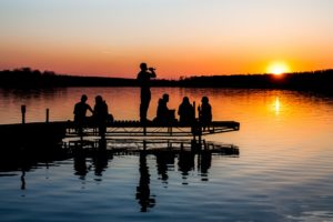 A group of people hanging out on a dock at sunset.